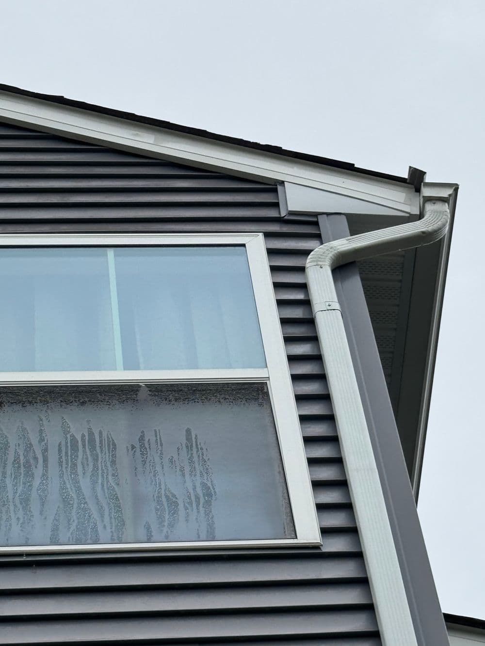 Close-up of a modern home's corner with a window and rain gutter, showcasing gray siding.