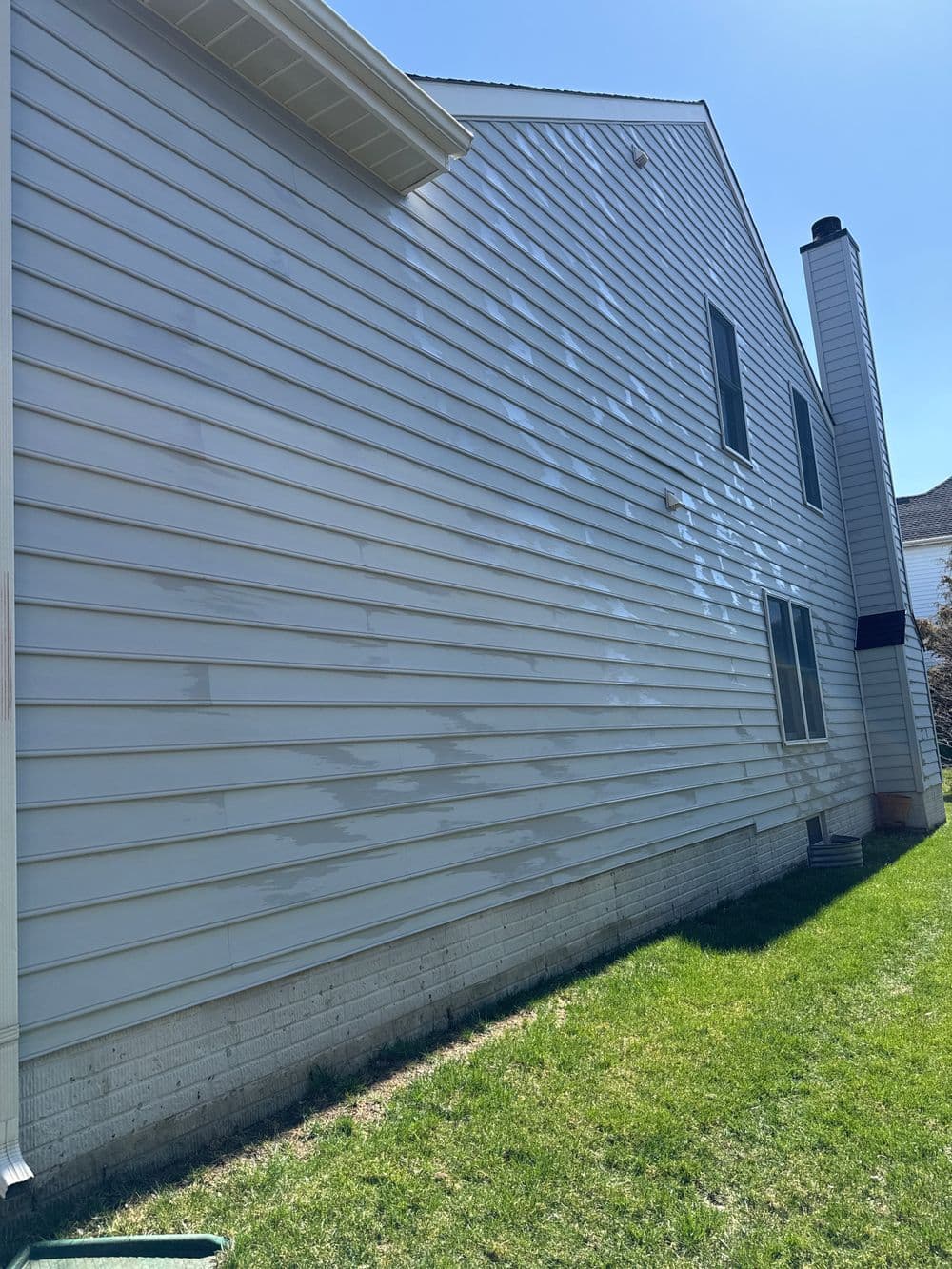 Side view of a residential home with freshly washed vinyl siding and green lawn.