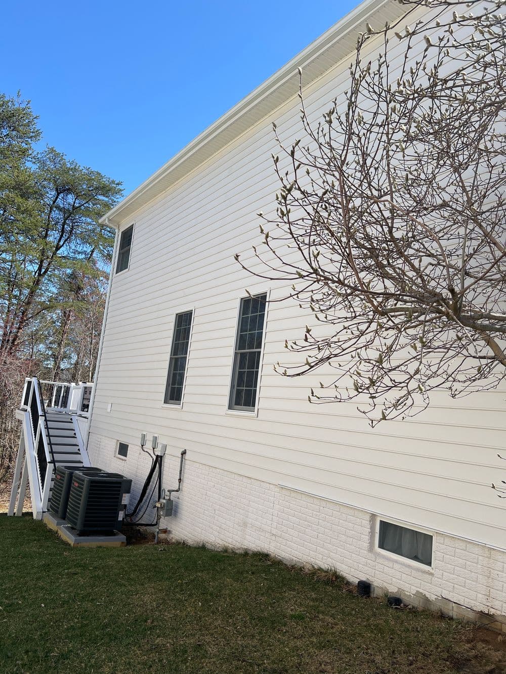 Modern home exterior with white siding, large windows, and stairs leading to the backyard.