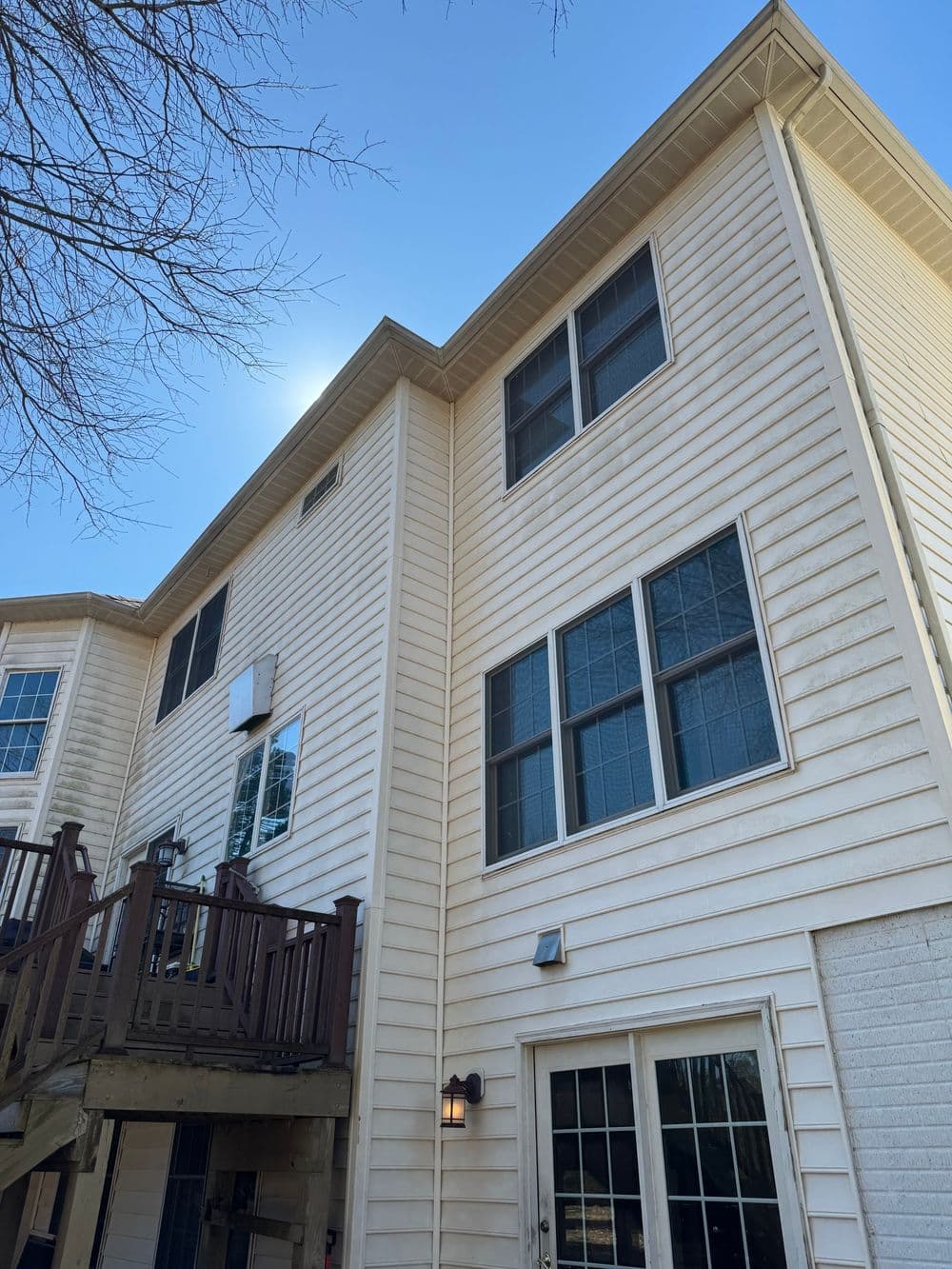 Two-story residential building with wooden deck, blue sky in the background.
